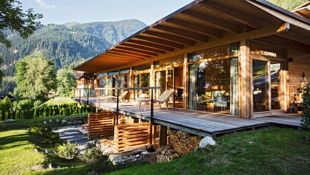 Una cabaña de madera con un balcón, ventanas amplias y vistas a un paisaje montañoso.