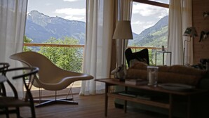Una sala moderna con vistas a las montañas, un sofá, una silla y una mesa con lámpara.