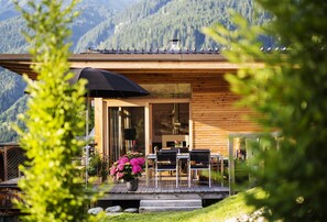 A wooden cabin with a deck, outdoor seating, and a view of mountains. - Alpenlofts (Bad Gastein)