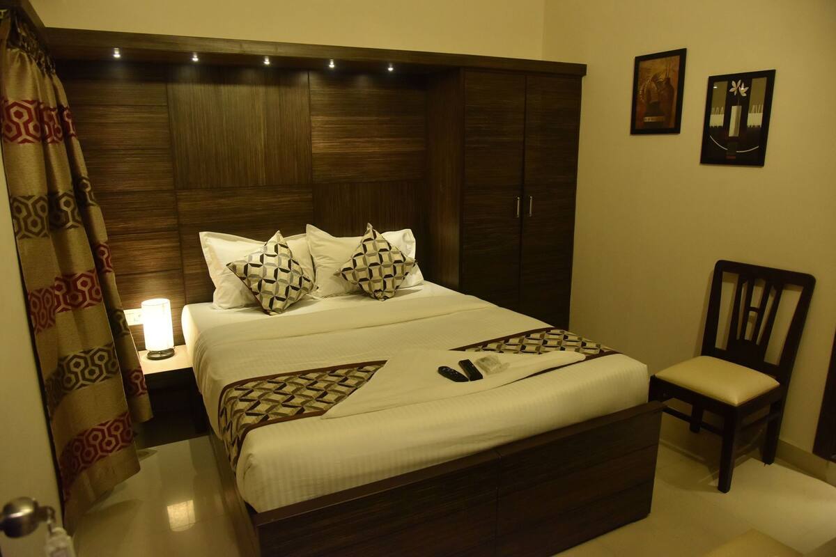 A hotel room with a large bed, a bedside lamp, a chair, and two framed pictures on the wall.