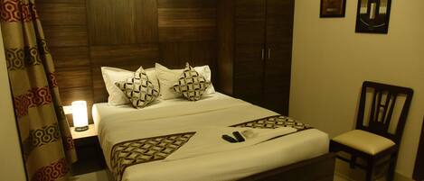 A neatly made bed with patterned pillows, a bedside lamp, and a wooden wardrobe.