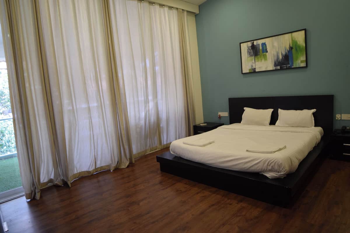 A bedroom with a bed, a nightstand, a painting on the wall, and a window with curtains.