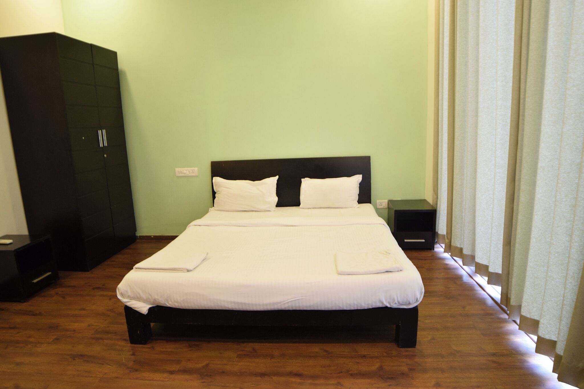 Una cama bien tendida con sábanas blancas, cabecera oscura y suelo de madera.