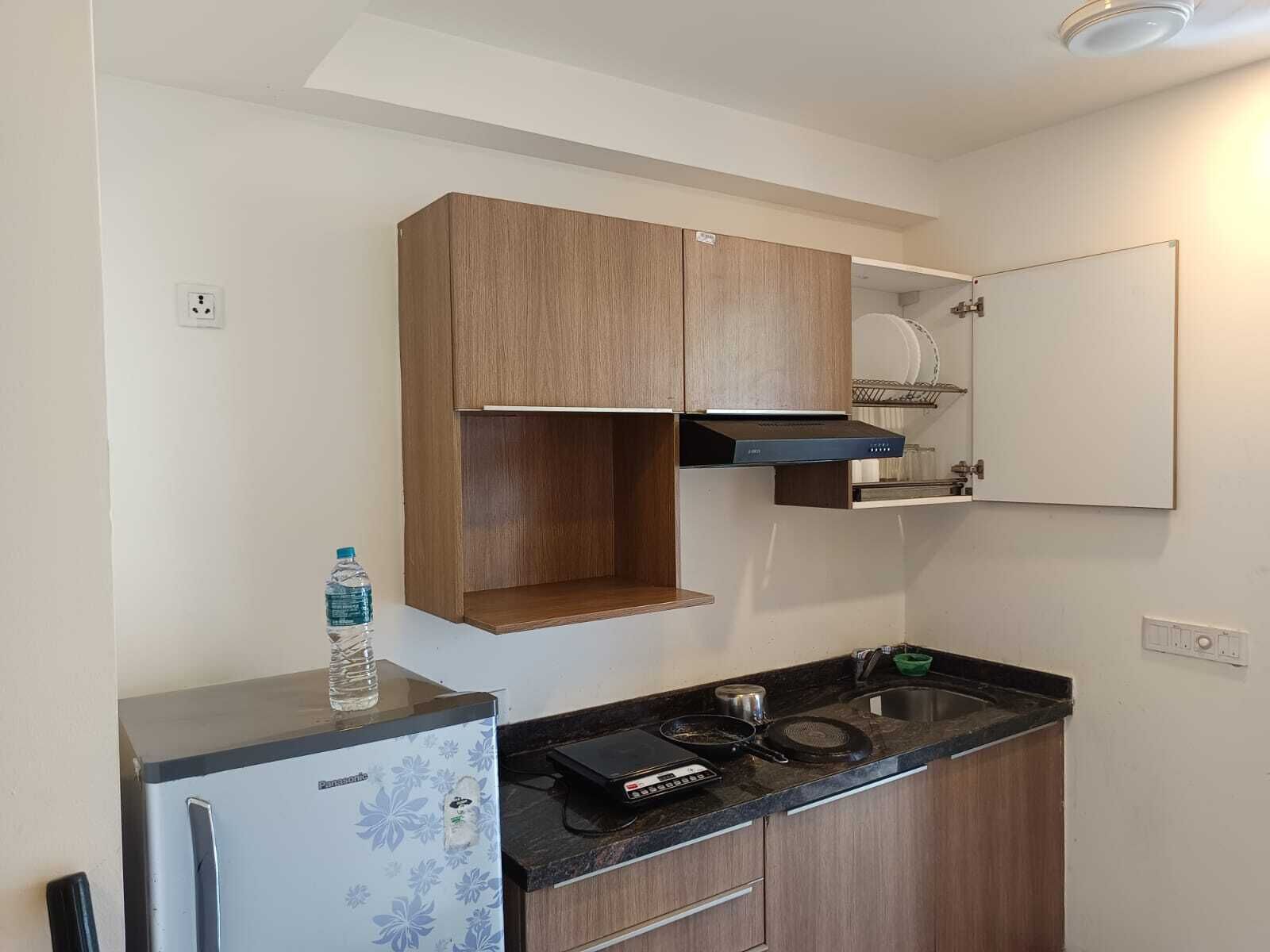 A compact kitchen with a refrigerator, a microwave, a sink, and wooden cabinets.