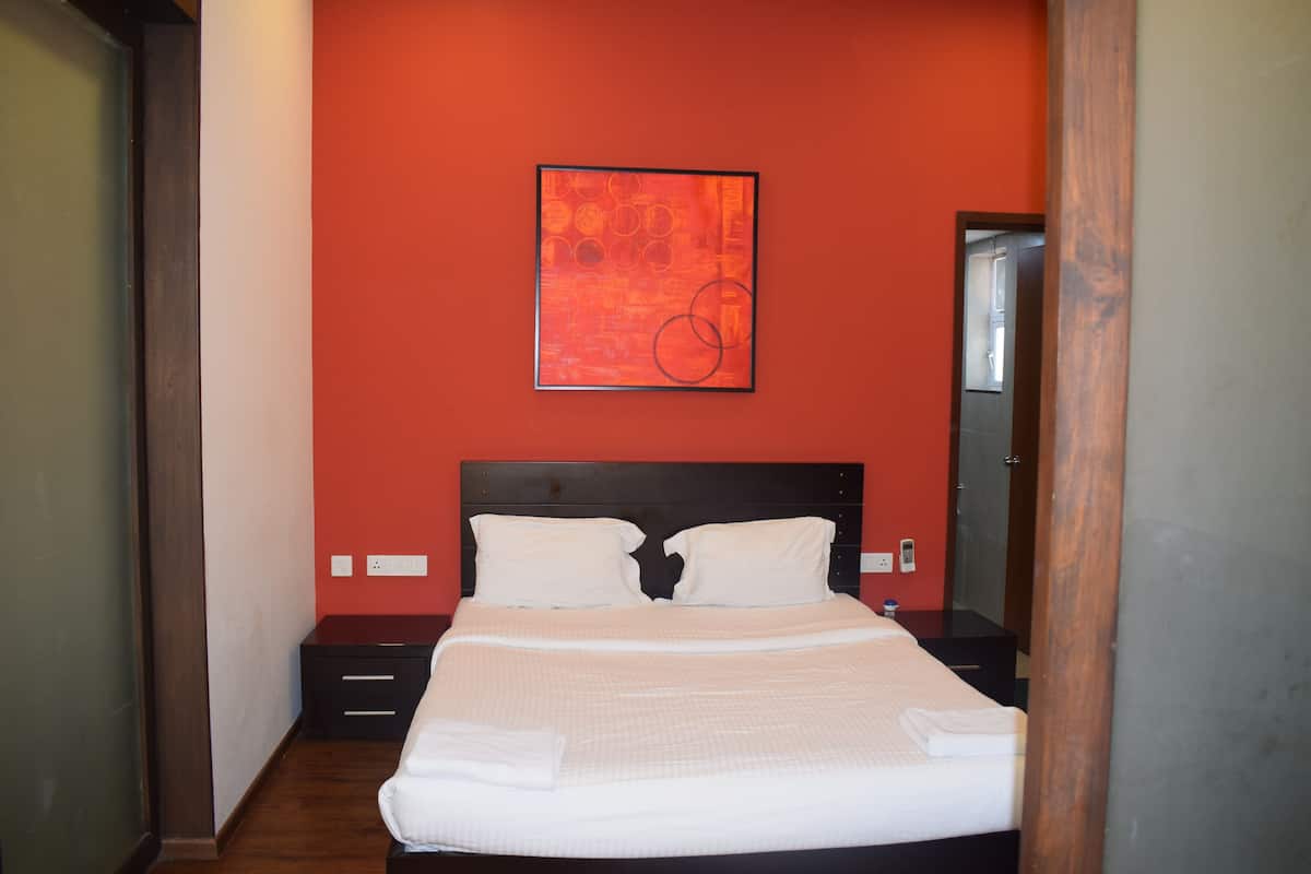 A neatly made bed with white linens in a room with red walls and a wooden headboard.