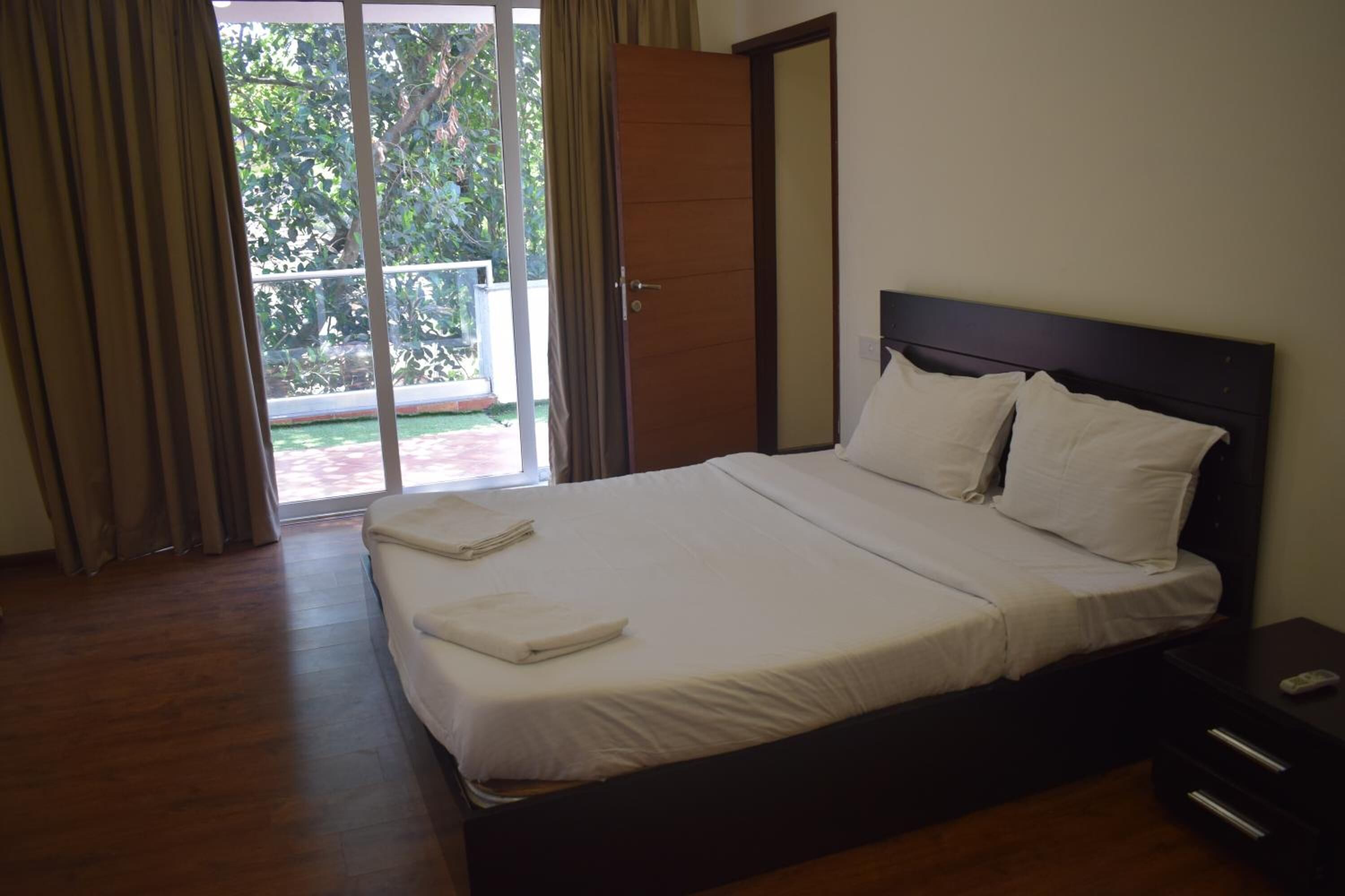 Cama bem arrumada com lençóis e almofadas brancos, cabeceira de madeira e mesa de cabeceira com controle remoto.
