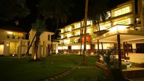 A multi-story hotel with a well-lit courtyard, palm trees, and a pool area. - The Eternal Wave by Krish Retreat (Calangute)