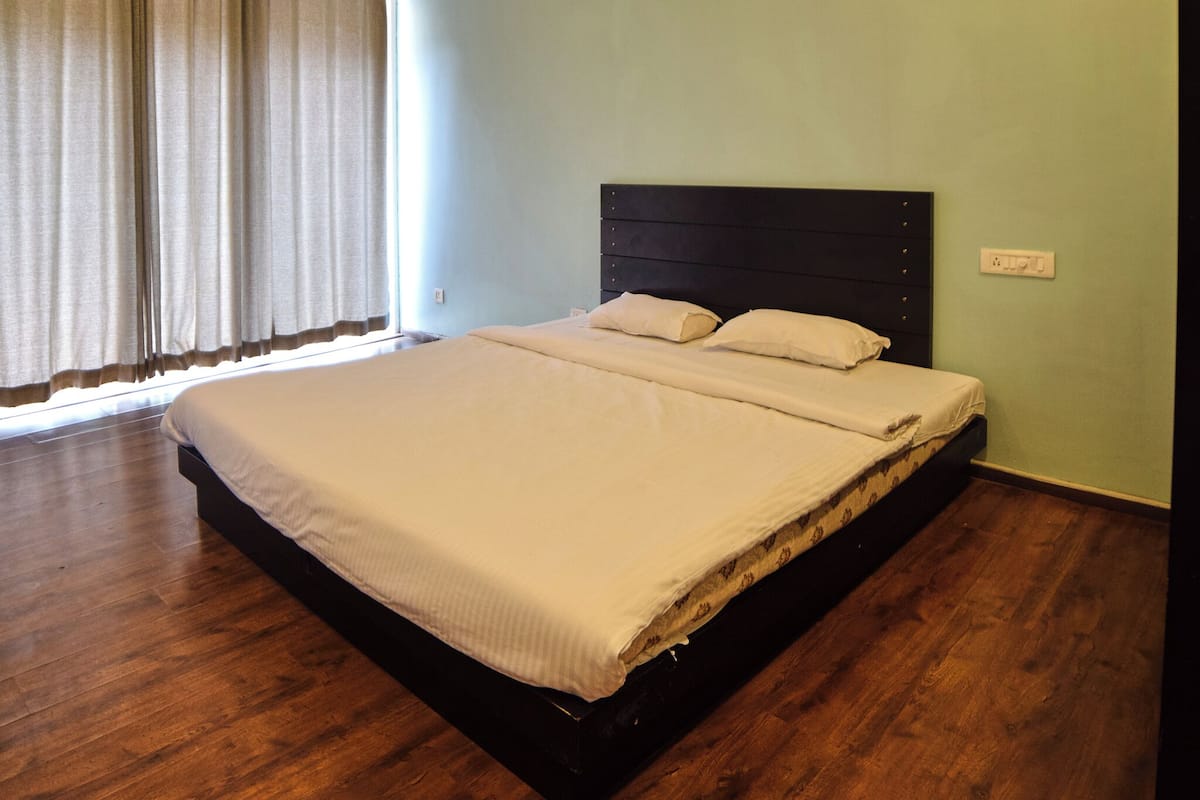 A single bed with a dark headboard in a room with light green walls and wooden flooring.