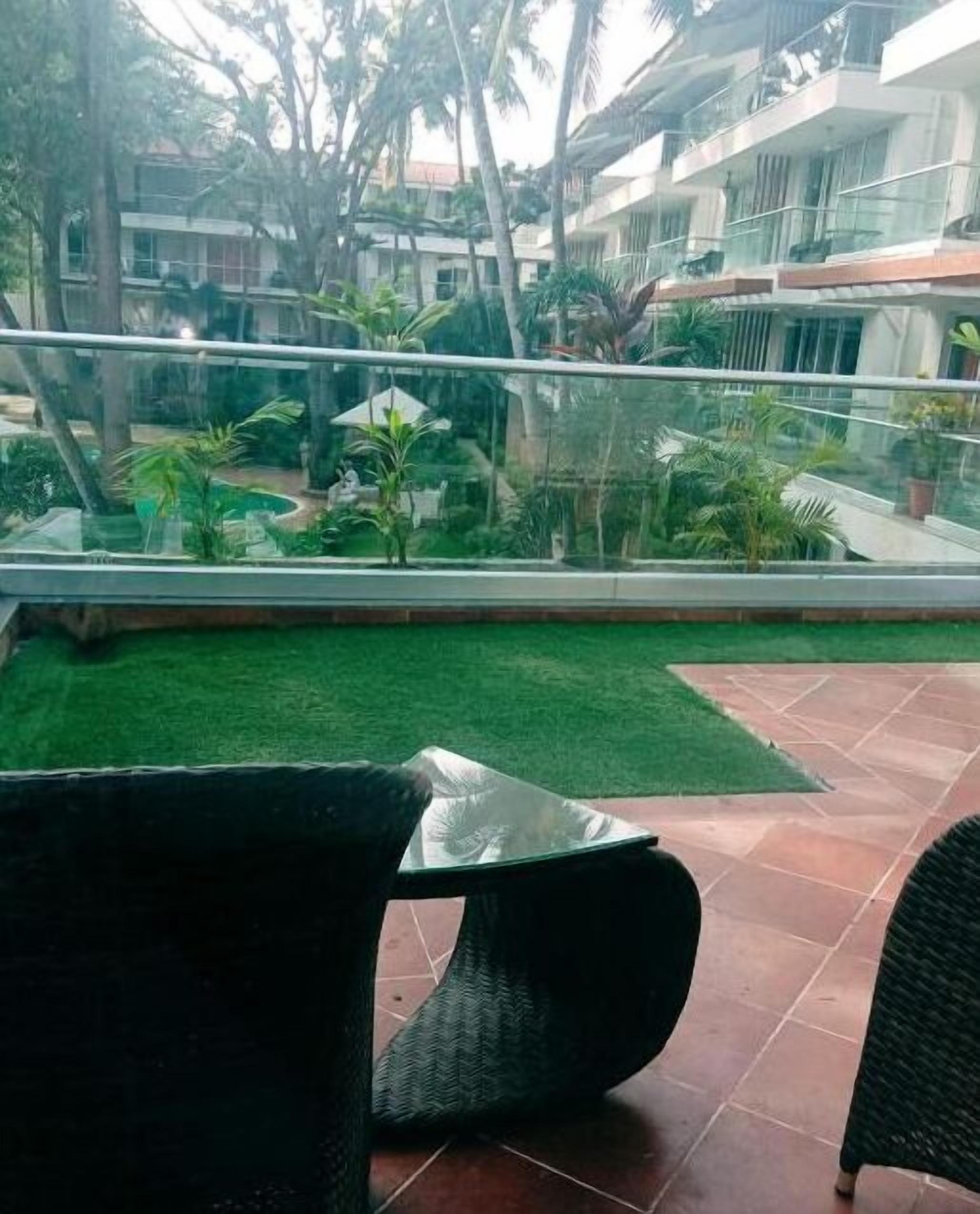 A terrace with a glass railing, green lawn, and wicker furniture.