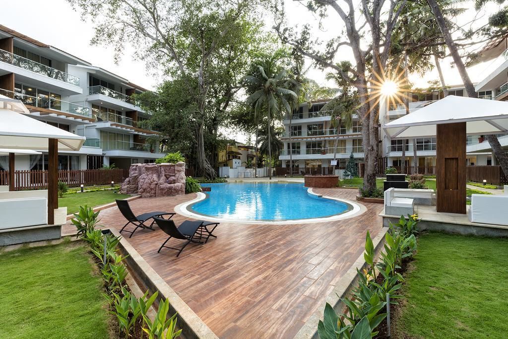 A swimming pool with lounge chairs, surrounded by a wooden deck and greenery, with multi-story buildings in the background.