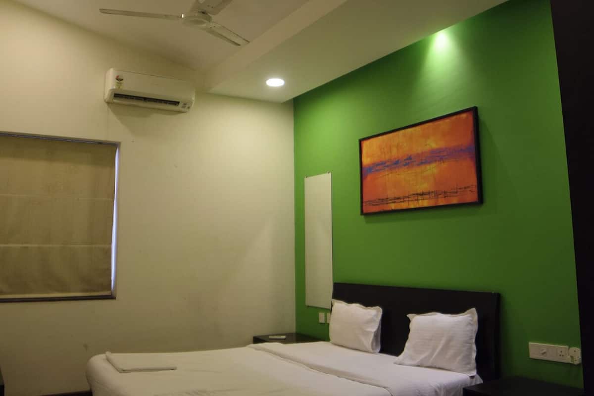 A bedroom with a bed, a ceiling fan, an air conditioner, a window with a blind, and a green wall with a painting.