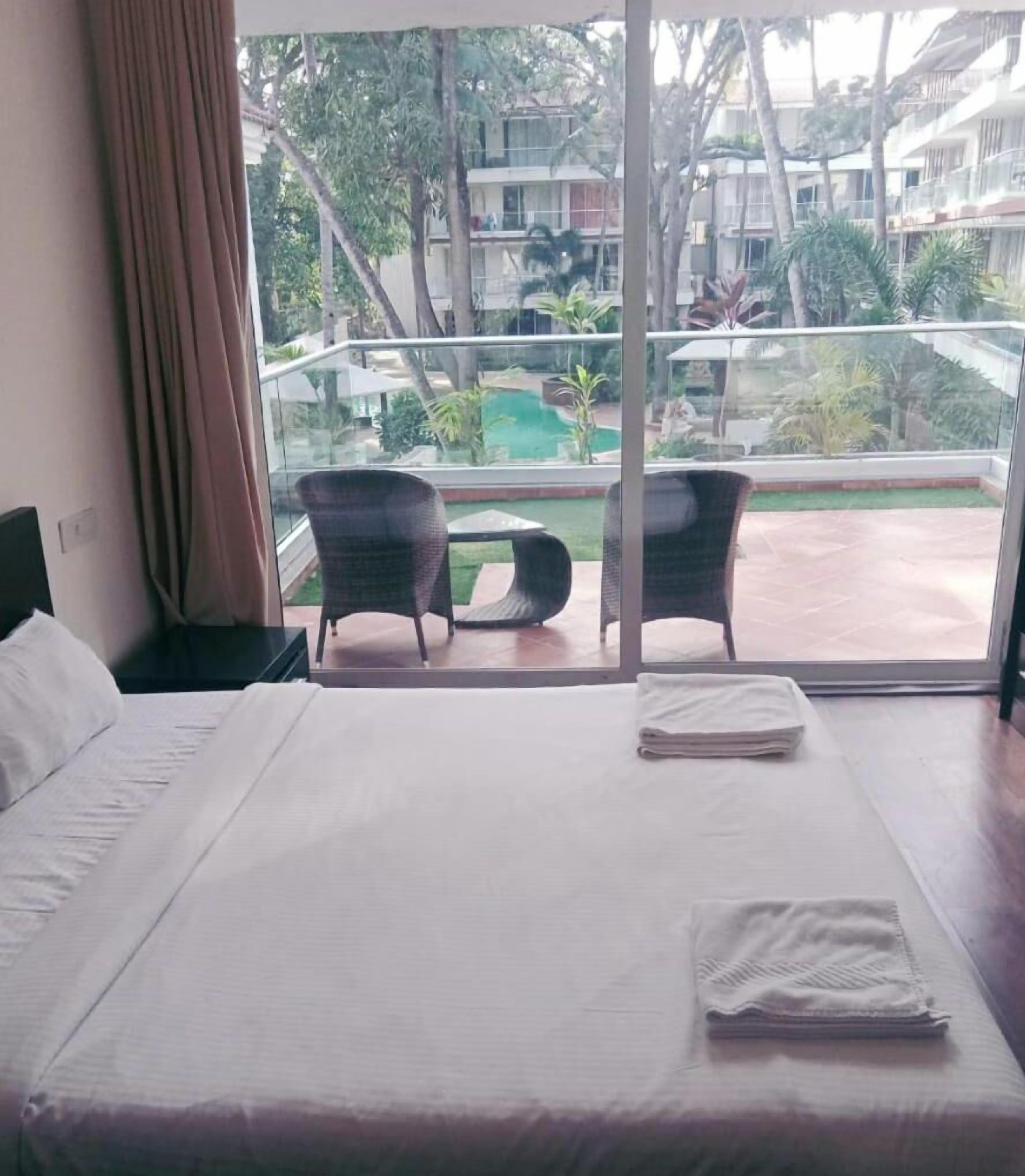 Hotelkamer met een groot bed, twee stoelen en uitzicht op een zwembad en groen.