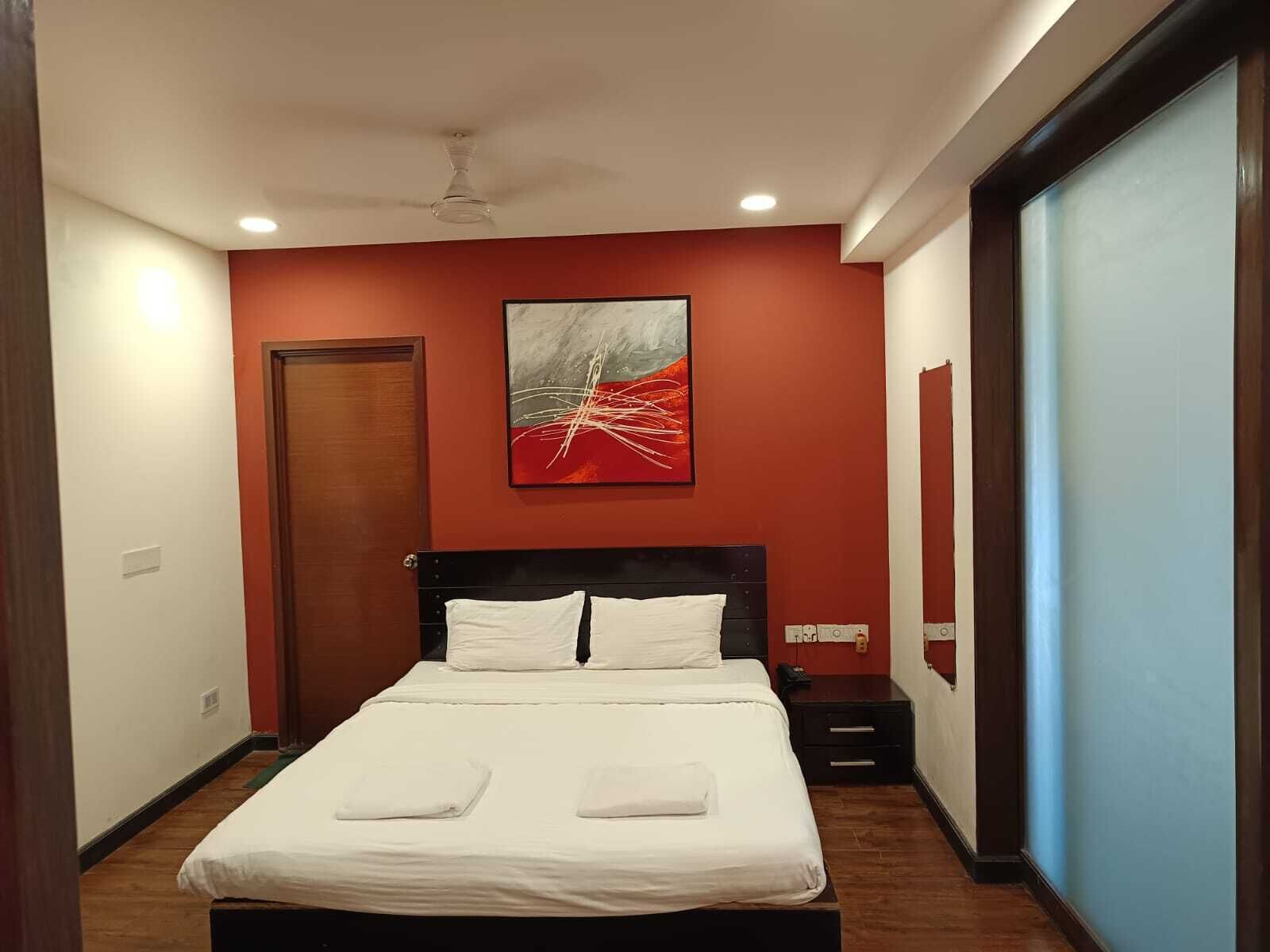 A hotel room with a bed, a ceiling fan, a painting on the wall, and a door.
