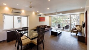 A spacious living area with a glass dining table, comfortable seating, and a large sliding glass door leading to a balcony. - The Eternal Wave by Krish Retreat (Calangute)