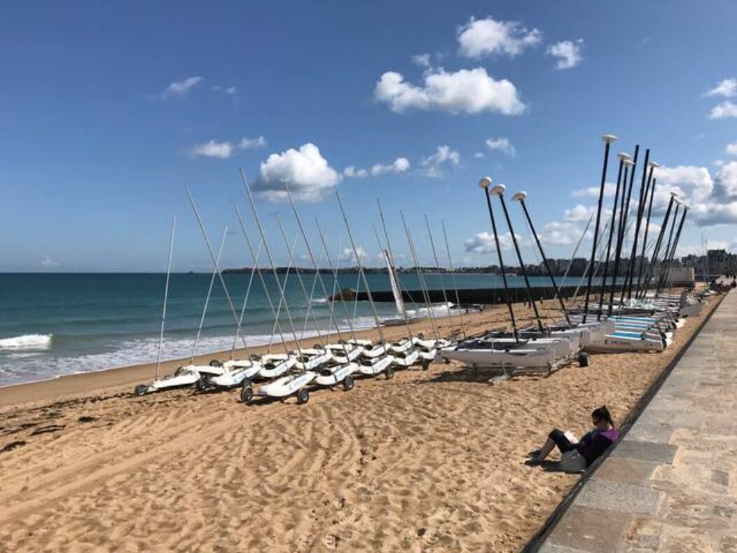 A beach with boats lined up on the sand and a person lying on the beach.