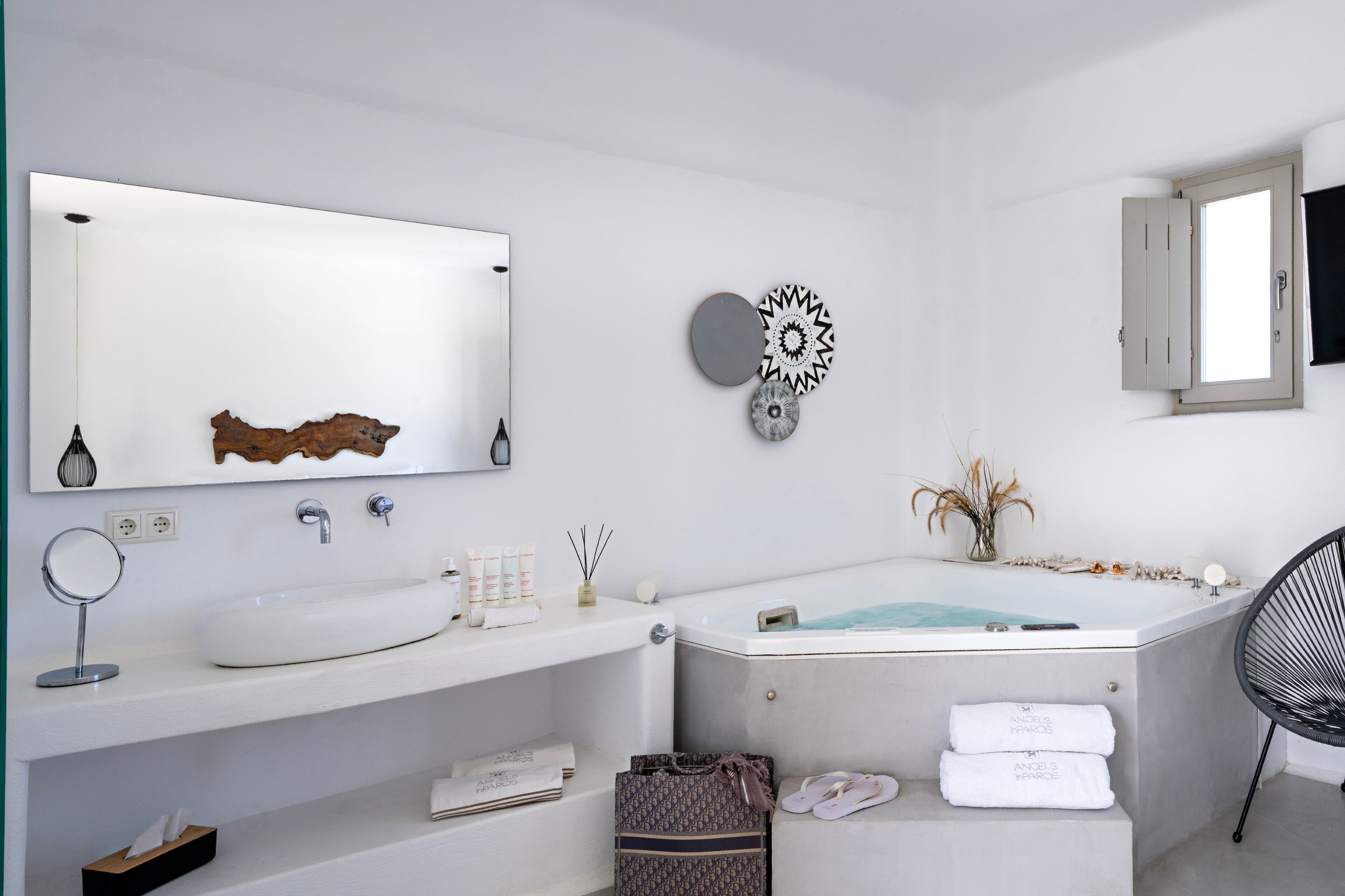 Ein modernes Badezimmer mit einem großen Spiegel, einem weißen Waschbecken und einer Badewanne. Handtücher, eine kleine Pflanze und ein dekoratives Wandbild sind ebenfalls vorhanden.