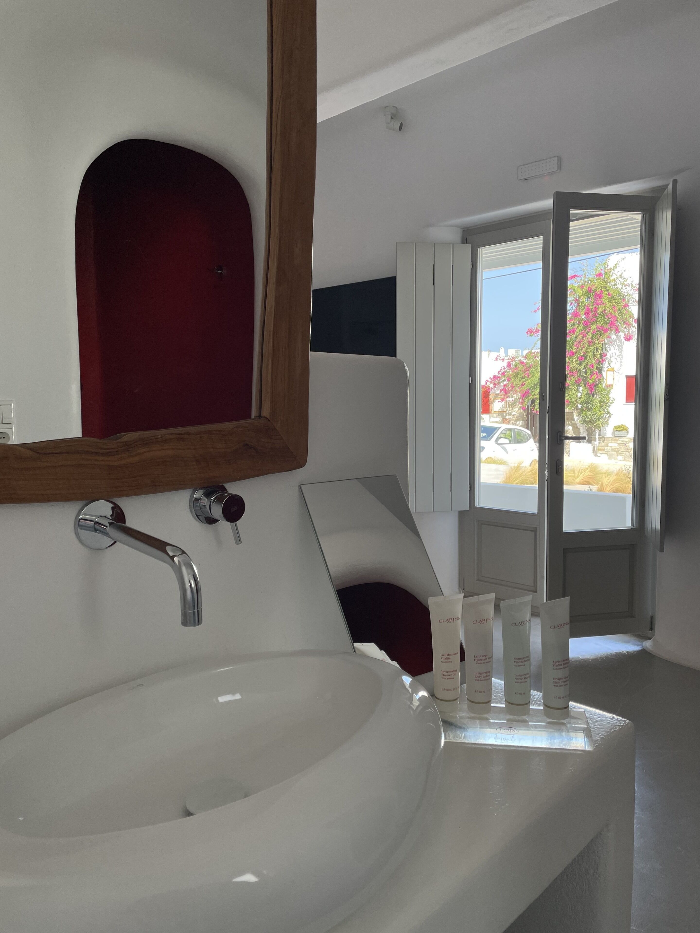 A modern bathroom with a large white sink, a mirror, and a red door.