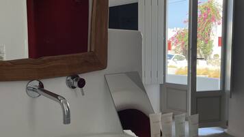 A modern bathroom with a large white sink, a mirror, and a red door.
