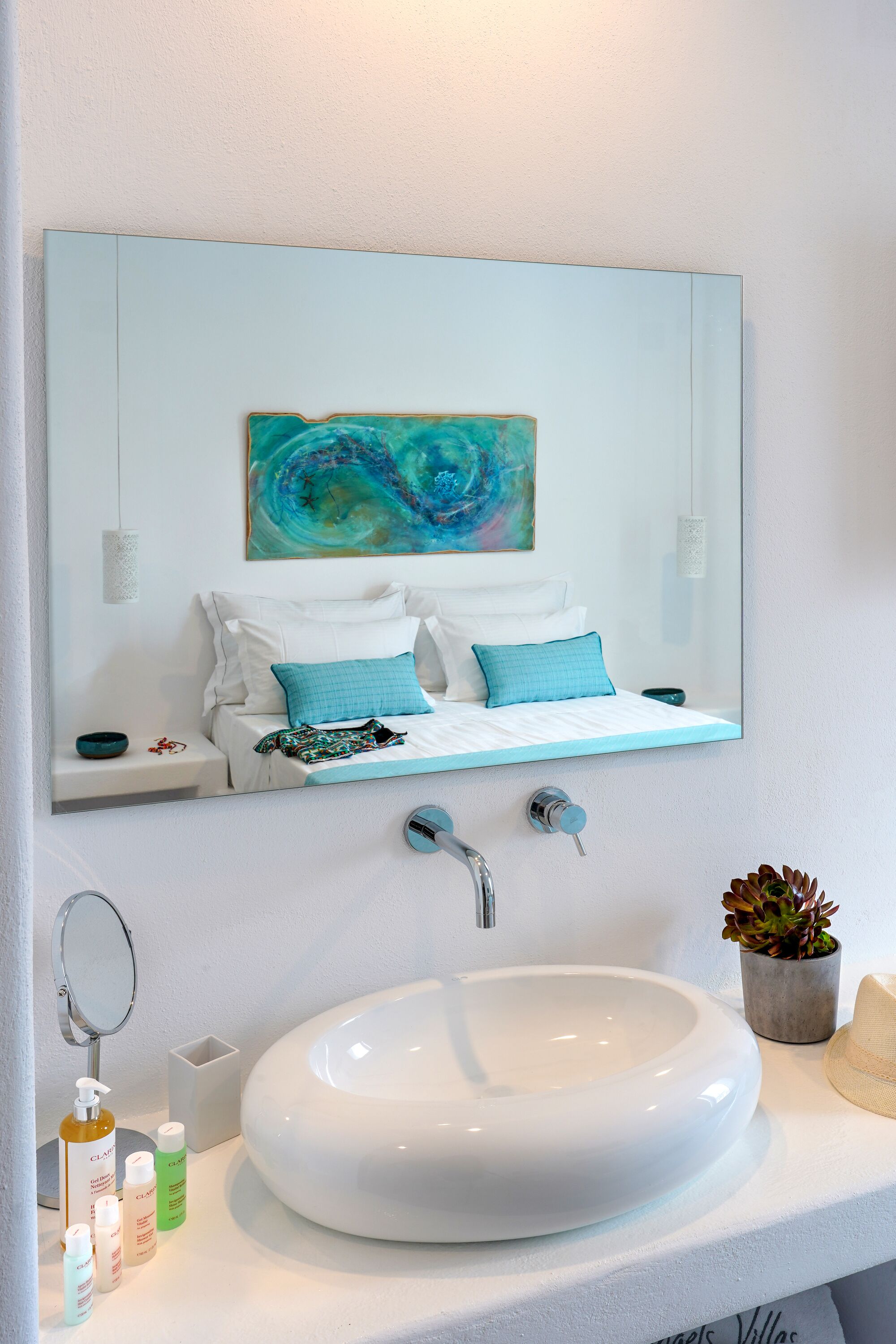 Un baño moderno con un espejo grande, un lavamanos blanco y una cama con ropa de cama azul y blanca.