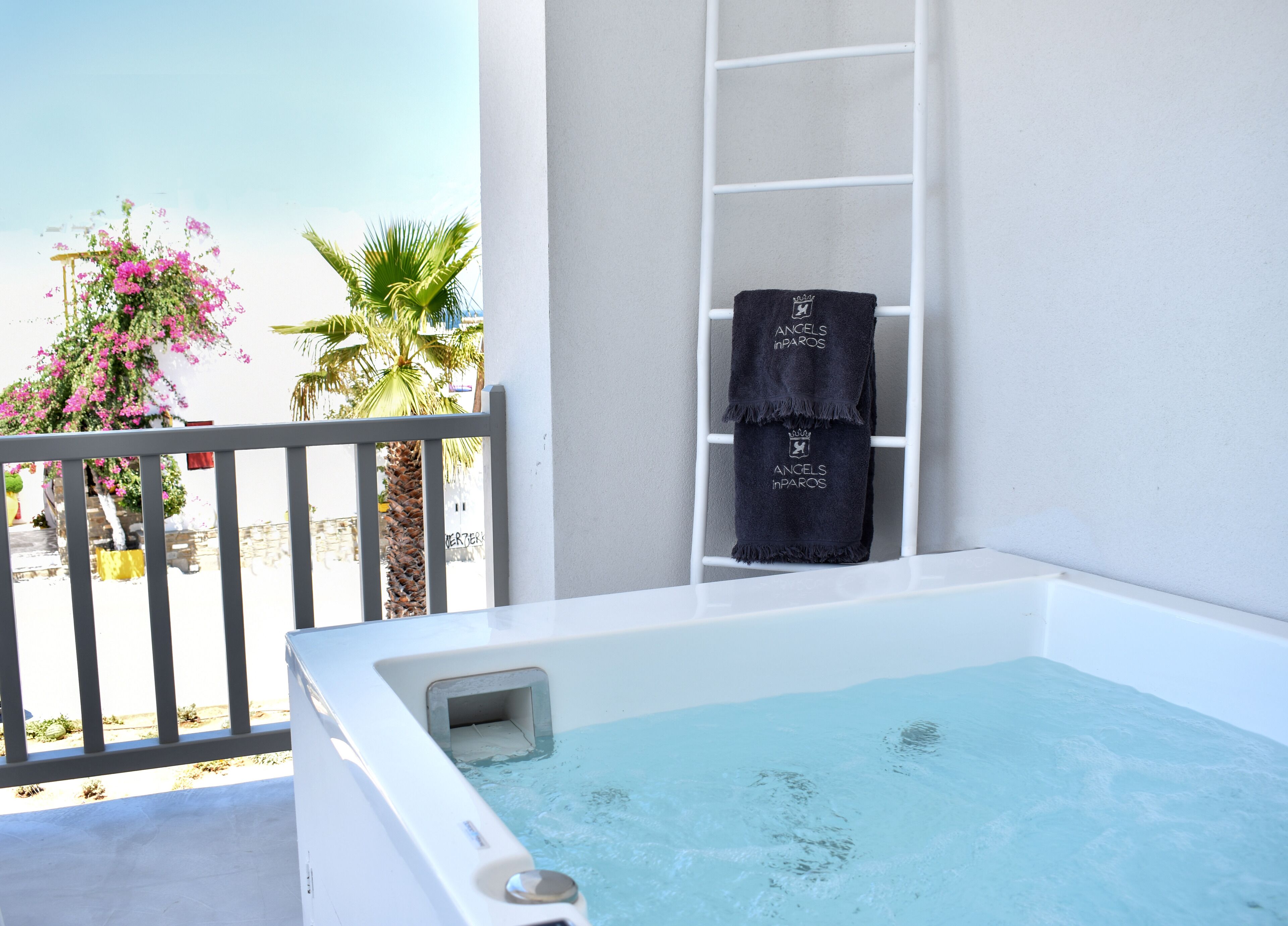 A white hot tub with a view of a balcony, a ladder, and a towel with "Angels in Paradise" text.