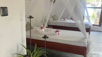 Una habitación con una cama bajo un dosel blanco, una planta en maceta y una mesita con una vela.