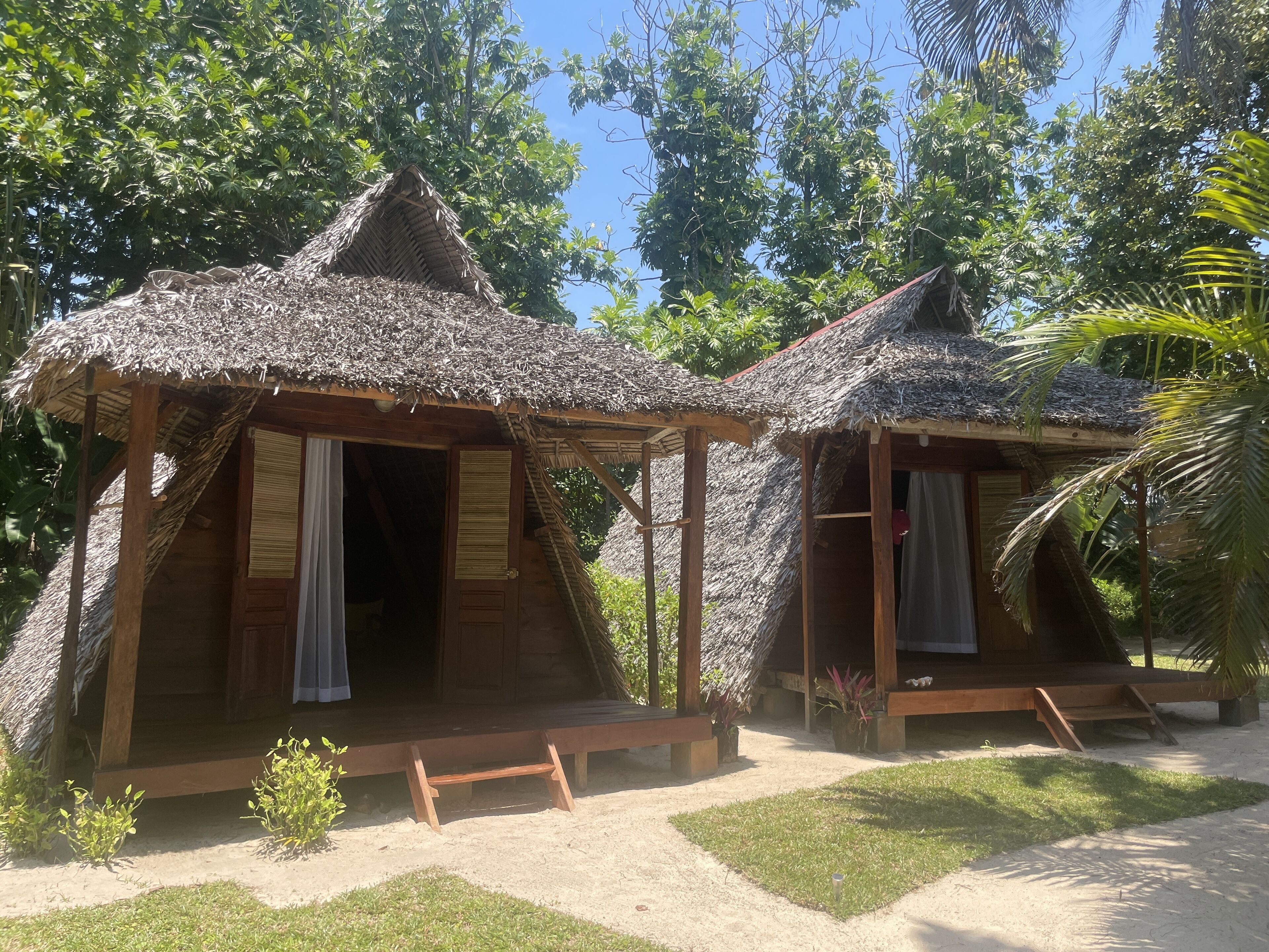 Dos cabañas con techo de paja y estructura de madera, cada una con un pequeño porche y una puerta.