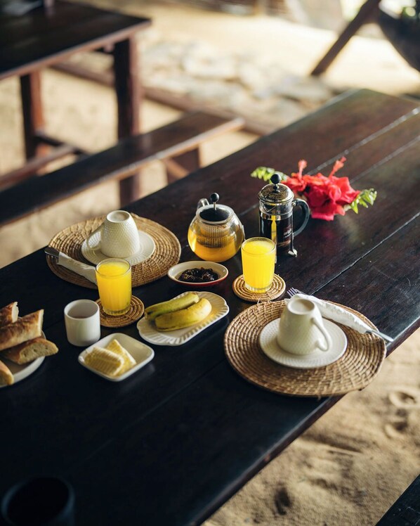 A wooden table set with breakfast items including bread, butter, and a jug of orange juice. - Aurora Lodge (Nosy Nato)