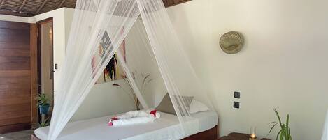 A bed with a white canopy, wooden headboard, and a small bedside table with a candle.