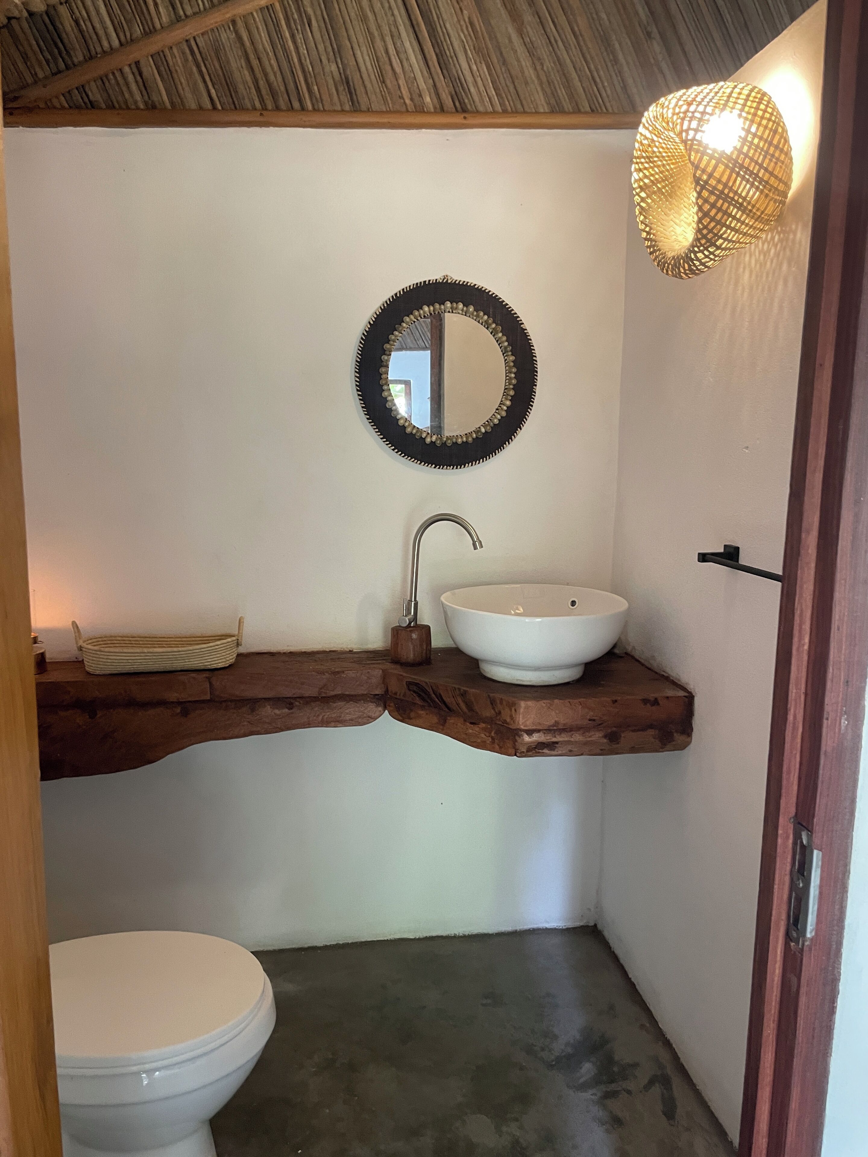 Une salle de bain avec un lavabo blanc, un meuble-lavabo en bois, un miroir rond et des toilettes.