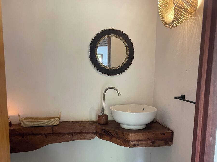 Une salle de bain avec un lavabo blanc, un meuble-lavabo en bois, un miroir rond et des toilettes.