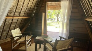 Una habitación acogedora y rústica con techo inclinado, muebles de madera y vistas a un jardín a través de un amplio ventanal.