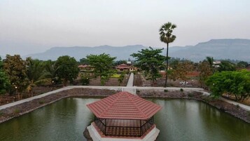 A pond with a gazebo in the center, surrounded by trees and a distant view of a building.