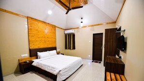 A bedroom with a bed, wooden headboard, bedside table, nightstand, and a TV mounted on the wall. - The Kanila Resort (Karjat)