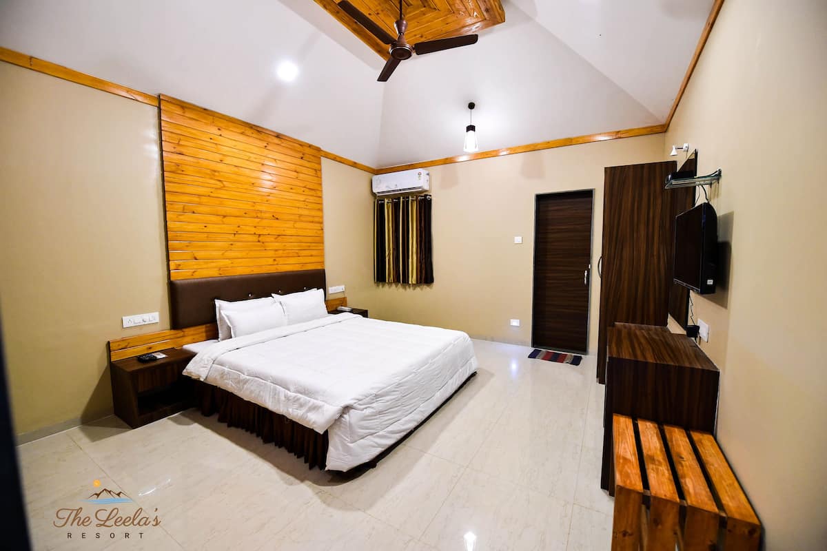 A bedroom with a bed, wooden headboard, bedside table, nightstand, and a TV mounted on the wall.