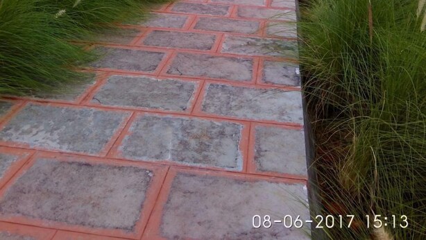 A stone pathway leading to buildings with red roofs, surrounded by lush greenery. - The Kanila Resort (Karjat)