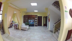 A spacious living area with a sofa, a television, and a dining table with chairs. - Hotel Aurora (Minturno)