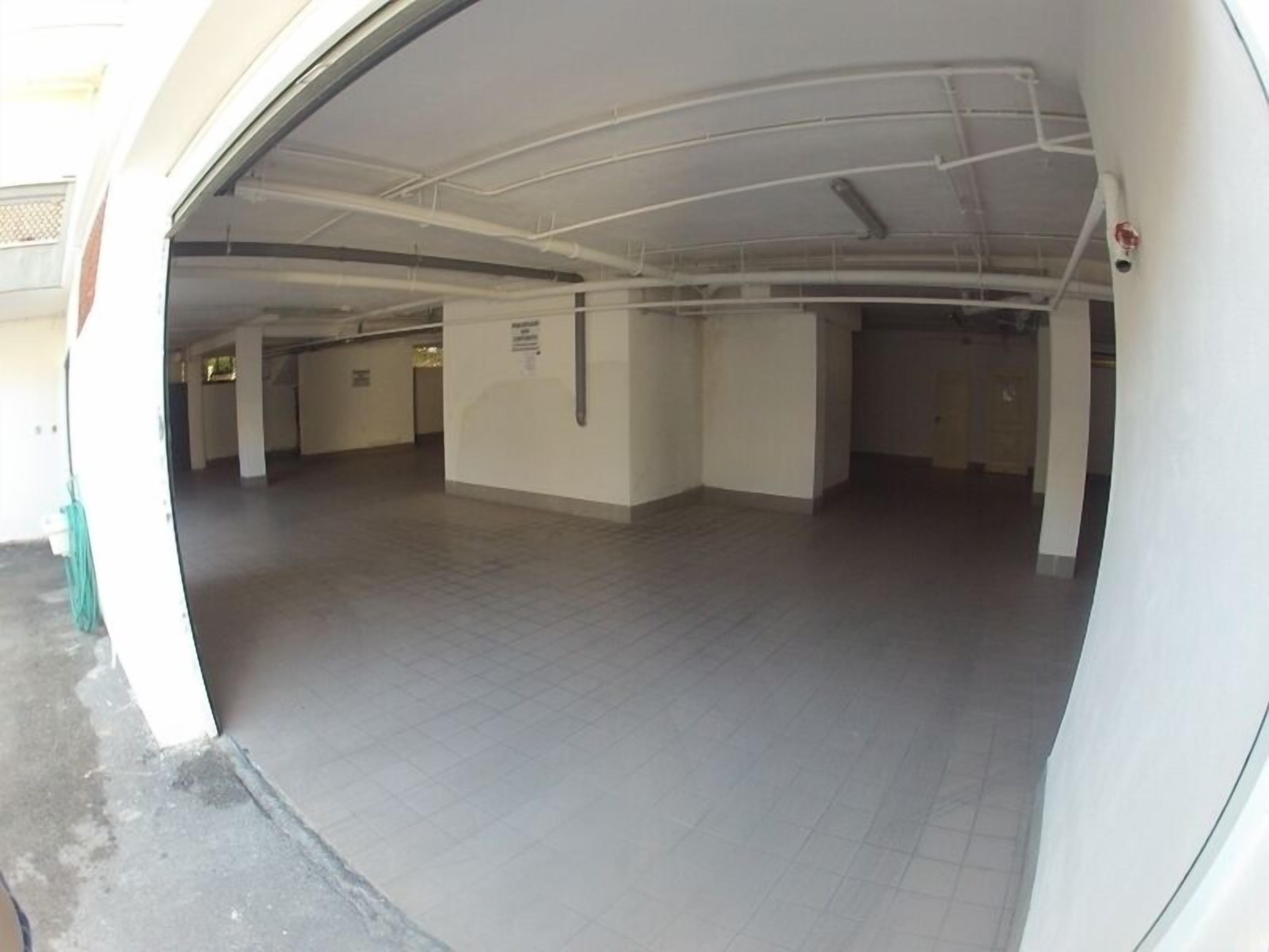 An indoor parking garage with a tiled floor, white walls, and ceiling pipes.