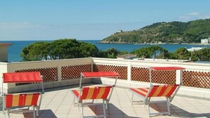 A rooftop terrace with red and yellow striped lounge chairs and a view of the sea and a hill. - Hotel Aurora (Minturno)