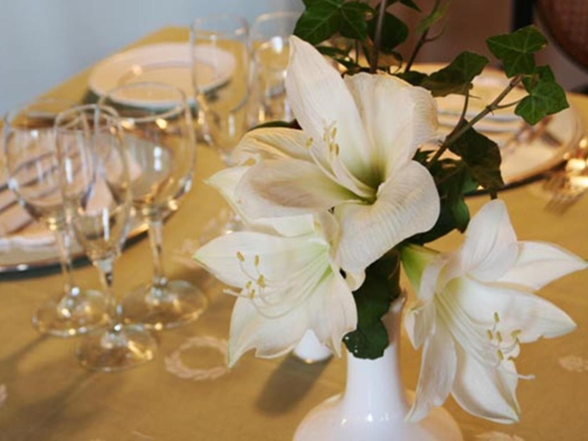 A table set with white flowers in a vase, surrounded by empty wine glasses and plates.