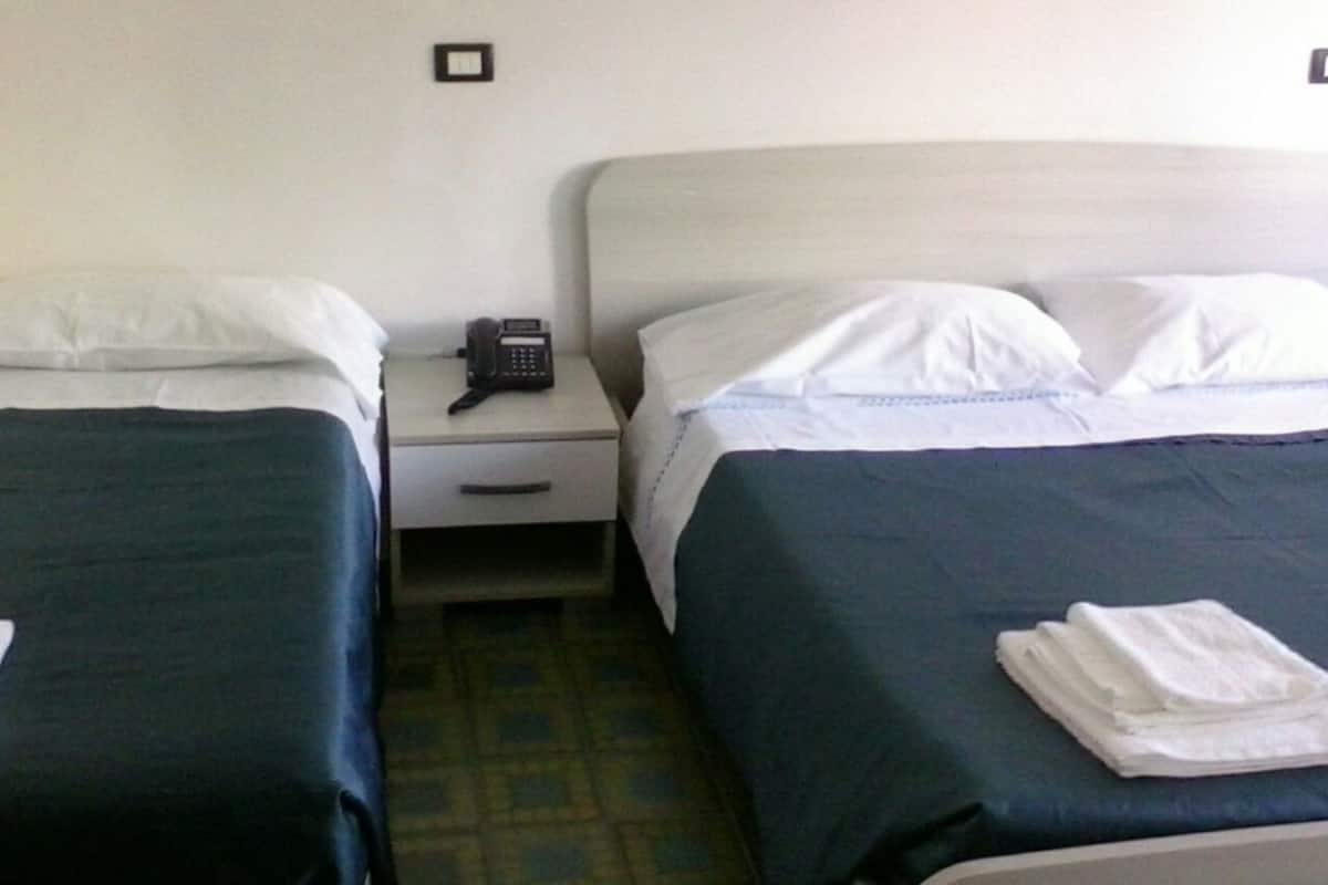 A hotel room with two single beds, a bedside table with a telephone, and a folded white towel on the bed.