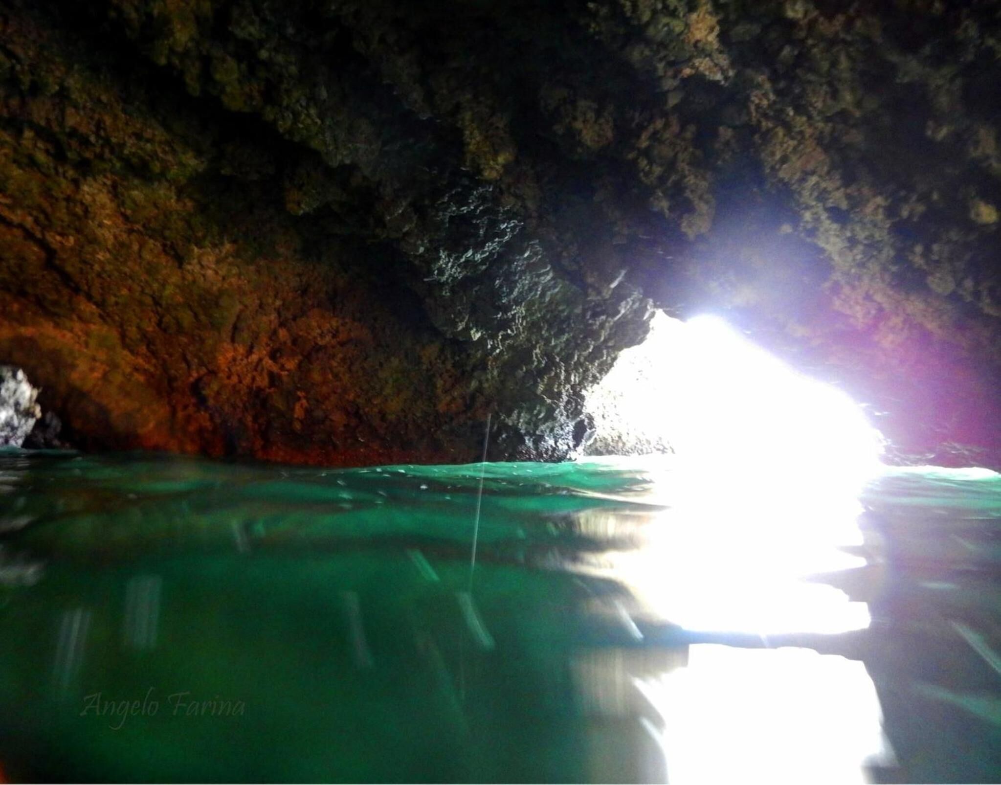 A cave entrance with water reflecting light, a rocky interior, and a person standing inside.