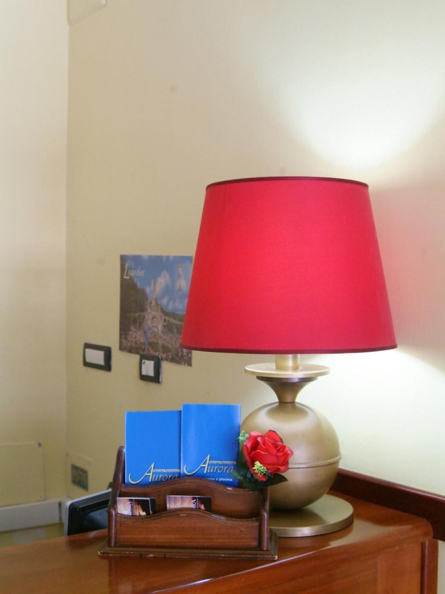A wooden desk with a red lamp, a blue card holder, and a small decorative flower.