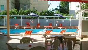 A poolside area with lounge chairs and umbrellas, a tiled floor, and a pool. - Hotel Aurora (Minturno)
