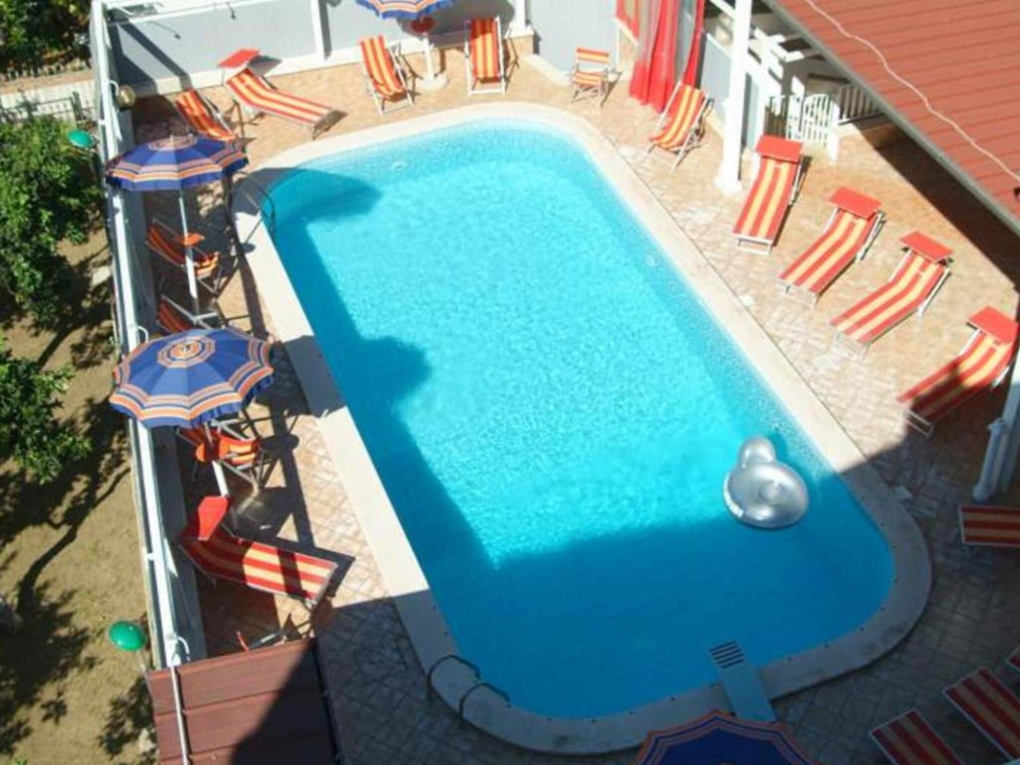 A rectangular swimming pool with a circular hot tub, surrounded by lounge chairs and umbrellas.
