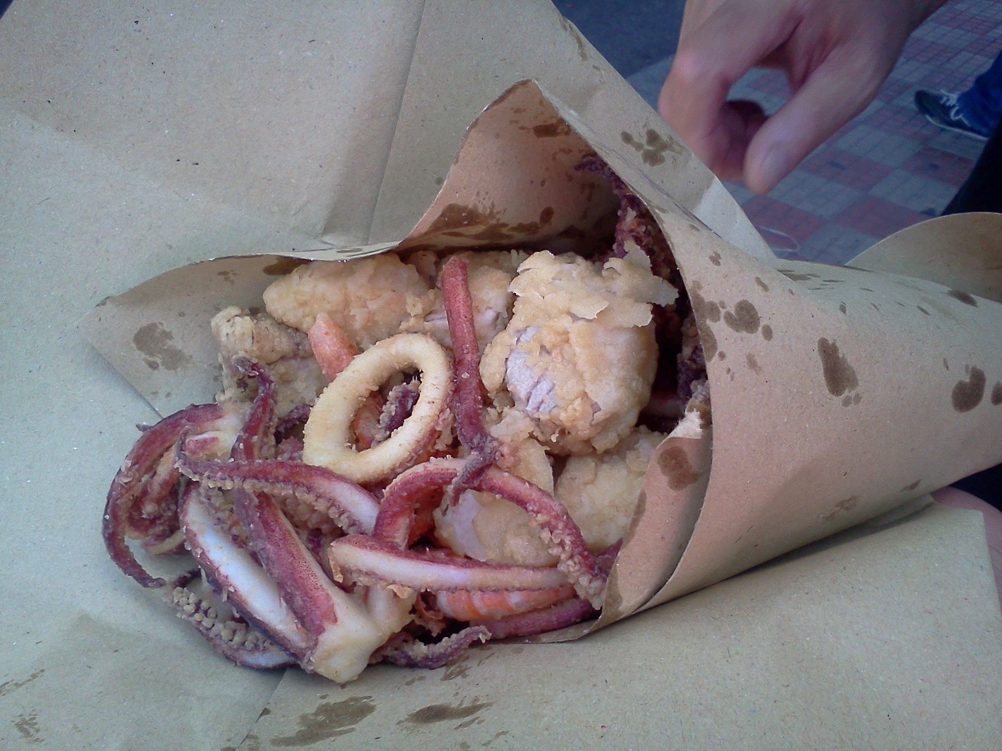 A paper cone containing fried seafood, including squid rings and shrimp.