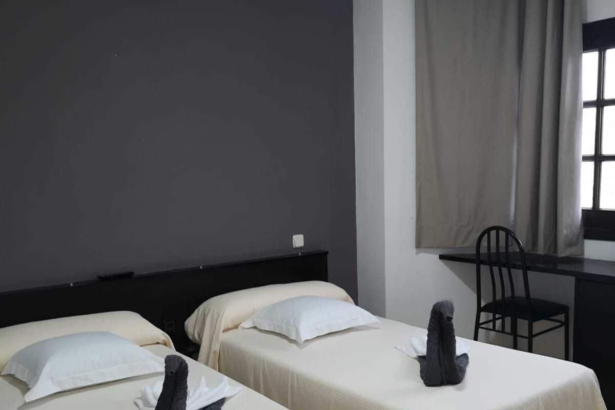 Habitación de hotel con dos camas, un escritorio, una silla y una ventana con cortinas.