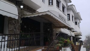 A two-story building with a white exterior, a covered entrance with a 'HOSTAL' sign, and a staircase leading to the entrance.