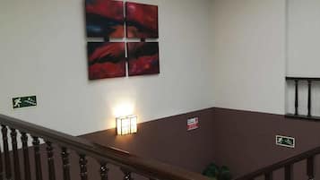 Een hotelhal met een houten trap, een plafondlamp en een schilderij aan de muur.