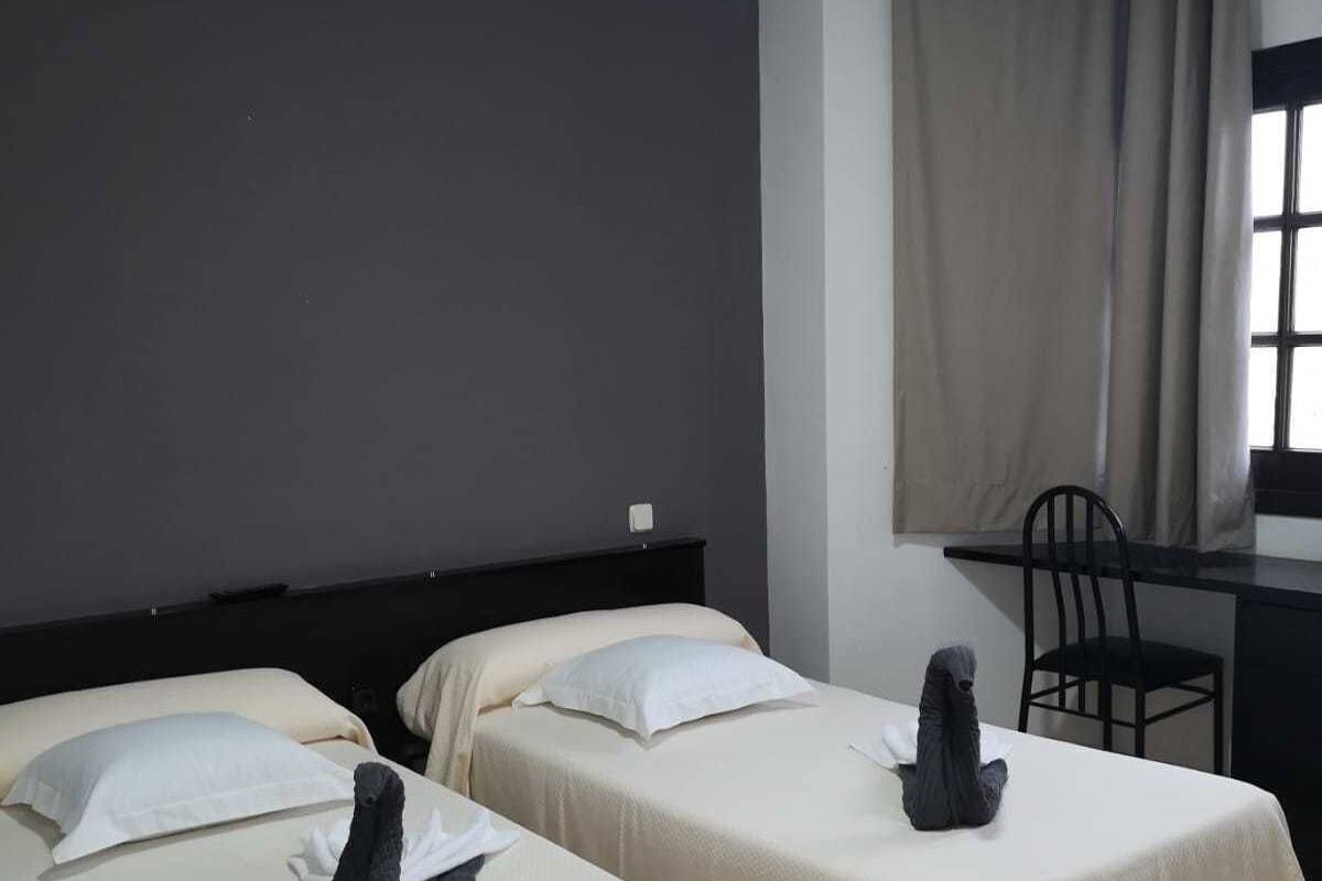 Habitación de hotel con dos camas, un escritorio, una silla y una ventana con cortinas.