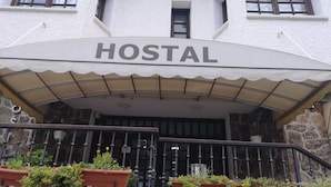 A building with a sign that reads "HOSTAL" above the entrance. There are potted plants on the balcony railing.